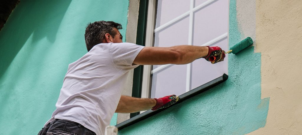 a worker paints the facade walls of a house with paint using a paint roller